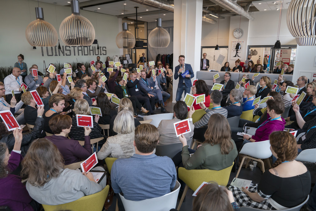 Moderator leading a room of participants holding up cards